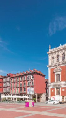 Panorama, Valladolid Plaza Belediye Başkanı Timelapse bayraklarıyla belediye binasının ön cephesini gösteriyor. Mavi gökyüzü ve şehrin göbeğindeki tarihi mimari. Yayalar bu merkez meydandan geçiyor..