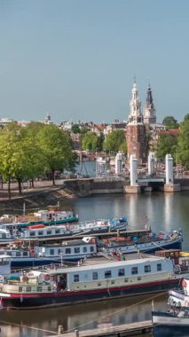 Amsterdam 'ın şehir panoramasının önünde Montelbaanstoren kulesi ve kanal boyunca uzanan şehir manzarası yer almaktadır. Eski kentin rıhtımında tarihi Hollanda evleri, mavnalar ve yüzen evler