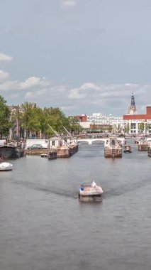 Amstel Nehri 'ndeki Amstel kilitlerinden geçen teknelerin panoramik görüntüsü. Opera binası ve Zuiderkerk kulesi arka planda görünüyor. Bulutlar gökyüzünü dolduruyor. Amsterdam, Hollanda