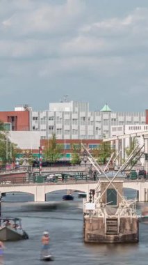 Amstel Nehri 'ndeki Amstel kilitlerinden geçen teknelerin zamanına göre görüntüsü. Opera binası ve Zuiderkerk kulesi arka planda görünüyor. Bulutlar gökyüzünü dolduruyor. Amsterdam, Hollanda