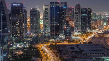 Jumeirah Lake Towers yerleşim bölgesi Dubai Marina yakınında gece geçiş timelapse gün havadan. Işıklı modern gökdelenler ve yukarıdan park