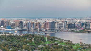 Güneş batarken Dubai Deresi ve Deira 'da arka planda deniz bulunan Park ve Mavi Nehir yakınlarındaki yeni modern binaların akşam manzarası Birleşik Arap Emirlikleri