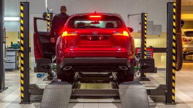 Tekerlek hizalaması için tekerlekli sensörlü araç servis istasyonunun zaman ayarlı atölyesinde kontrol ediliyor. Araba asansörde hareket ediyor