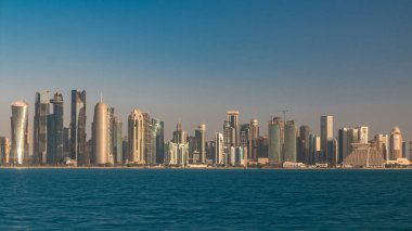 Katar 'ın Doha şehrinin ufuk çizgisi sabahın erken saatlerinde güneşin zengin ılık renkleri cam gökdelenlerden yansıyor..