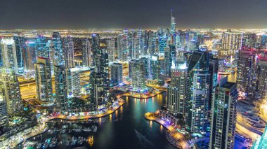 Dubai Marina 'da yatlar ve gece gündüz hava geçiş panoramik zaman dilimi. Mavi gökyüzü ile açık bir akşamda parlak ışıklar ve en yüksek gökdelenler. Gün batımından sonra yukarıdan görünüm