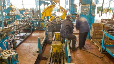 Traktör motoru, traktör fabrikasının üretim hattına monte edildi. Üniformalı işçiler taşıyıcıya dişli parçaları yüklerler