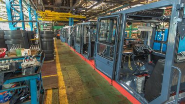 Konveyör montajı, traktörün gövdesini büyük endüstriyel fabrika zaman diliminde sahneleyecek. Kabin montajı, kurulum parçaları özel bir masada.