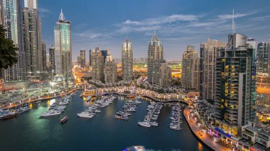 Dubai Marina gezinti güvertesi ve kanalı, gün batımından sonra Dubai, BAE 'de yüzen yatlar ve teknelerle hava üzerinden gece gündüz geçiş zamanı. Modern kuleler ve yukarıdan gelen trafik
