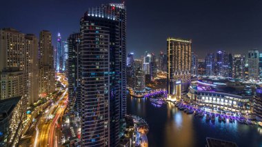 Dubai Marina 'nın gece gündüz aydınlanması. Hava geçiş zamanı, BAE. Modern gökdelenler ve konut binaları. Yapay kanal şehrindeki alışveriş merkezinin yakınındaki yatlar ve tekneler.