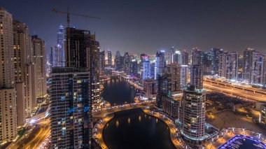 Günden geceye güzel bir hava manzarası. Dubai, BAE 'de gün batımından sonra yüzen yatları ve tekneleri olan Dubai Marina gezinti ve kanallarının panoraması. Modern kuleler ve yoldaki trafik.