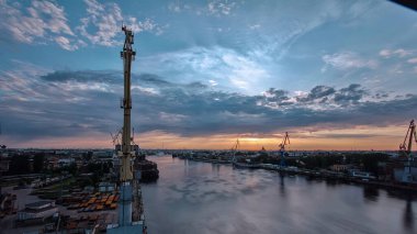 Shipyard with historical cranes in the industrial part on a riverside during sunrise aerial timelapse. Plants and factories around. Colorful sky at the morning