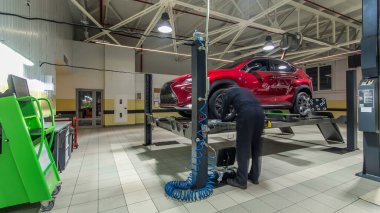 Tekerlek hizalaması için tekerlekli sensörlü araç servis istasyonunun zaman ayarlı atölyesinde kontrol ediliyor. Araba asansörde hareket ediyor