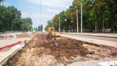 Tramvay rayları onarımı ve bakımı olan bir yol inşaatı. İnşaat alanında çalışan endüstriyel makineler zaman ayarlı. Buldozer yerde çalışıyor.