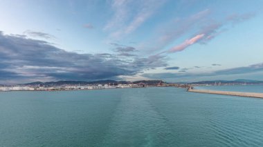 Gün batımında açık denizde yelken açan gemiden dalgalı ve limanlı deniz manzarası. Barselona kıyısı, İspanya