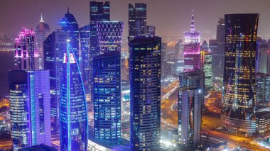 Batı Körfezi bölgesinin ufuk çizgisi Doha 'da günden geceye geçiş zamanı, Katar. Günbatımından sonra modern gökdelenlerin çatıdan görünüşü aydınlandı. Yolda trafik vardı.