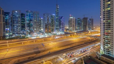 Sheikh zayed road ve metro hattı üzerinde Jumeirah lakes towers gökdelenler gün gece geçiş timelapse trafik için havadan görünümü.