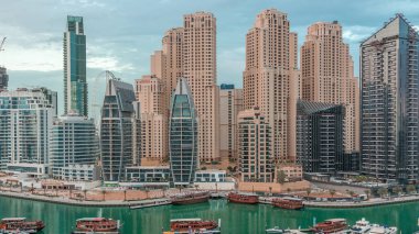 Dubai Marina körfezindeki iskeleye park etmiş lüks yatlar. Gece gündüz şehrin hava manzaralı geçiş zamanı. Etrafında aydınlık kuleler ve gökdelenler var. Yağmurlu bulutlar ve şimşekler.