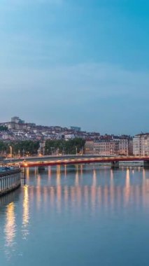Lyon 'daki Saone Nehri' nin üzerindeki Palais du Justice Köprüsü 'nde, günden geceye geçiş. Rıhtımdaki aydınlık binalar gün batımından sonra suya yansıyor.