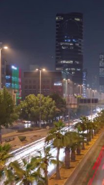 Suudi Arabistan, Riyad 'daki ikonik bükümlü gökdelenle King Fahd Yolu' ndaki yoğun karayolu trafiğinin hava takvimi görüntüsü. Aydınlanmış sokaklar ve ağaçlar. Dünyanın en uzun sekizinci büküm kulesi..