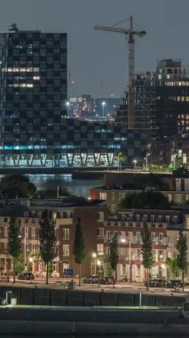 Geceleri Katendrecht yarımadasının panoramik zaman çizelgesi, Hollanda Rotterdam 'daki Maashaven limanı ve nehri. Aydınlatılmış şehir silüeti, modern gökdelenler ve geleneksel rıhtım evleri
