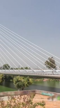 İspanya 'nın Sevilla kentindeki Guadalquivir Nehri' nin üzerinden geçen uzun kolon ve çelik kablolu Alamillo Köprüsü. Açık mavi gökyüzü altında yoğun trafik ile modern süspansiyon tasarımının hızlandırılmış zamanlaması.