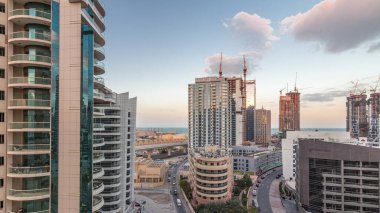 Dubai Marina 'da aydınlık gökdelenler ve gece gündüz gezinti güvertesi geçiş zamanı. Yol trafiği olan modern kuleler ve tekneler. Birleşik Arap Emirlikleri