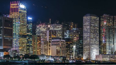 Günümüz modern gökdelenlerinde ışıldayan pencereleri olan Hong Kong 'un silueti Victoria Limanı' ndan gece geçişi. Rıhtımın manzarasını kapat. Gün batımından sonra güzel gökyüzü