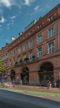 Toulouse, Occitanie, Fransa 'da Rue de Metz' in zaman çizelgesini gösteren panorama, tarihi cepheleri, dükkanları, kafeleri, trafiği ve mavi bulutlu gökyüzünü gösteriyor. Şehrin göbeğinde canlı bir şehir manzarası