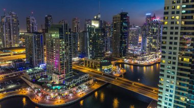 Dubai Marina gezinti güvertesi ve kanalı, gün batımından sonra Dubai, BAE 'de yüzen yat ve tekneler ile gündüz hava manzaralı. Modern kuleler, köprü ve trafik yukarıdan geliyor.