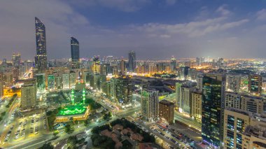 Abu Dabi gökdeleninin modern şehir mimarisi günden geceye geçiş havası, BAE. Aydınlatılmış gökdelenler ve yol trafiği. Abu Dabi başkenti ve ikinci en kalabalık şehirdir.