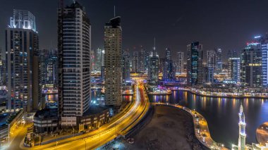 Dubai Marina gezinti güvertesi ve kanalı, gün batımından sonra Dubai, BAE 'de yüzen yatlar ve teknelerle hava üzerinden gece gündüz geçiş zamanı. Modern kuleler ve yol trafiği