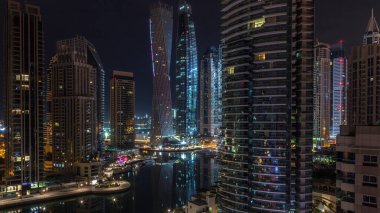 Dubai Marina konutlarının ve ofis gökdelenlerinin panoramik hava manzarası ve tüm gece boyunca deniz kenarında yanıp sönen ışıklar. Yüzen tekneler ve yatlar