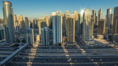 Dubai Marina gökdelenleri, güneş doğarken Dubai 'de JLT' den gündüz saatlerine kadar gökdelenler. Aydınlatılmış uzun gölgeli modern kuleler aşağı doğru ilerliyor ve Şeyh zayed yolunda trafik var..