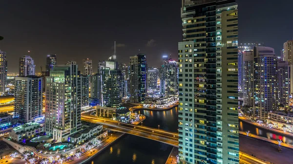 Dubai Marina gezinti güvertesi ve kanalı, Dubai, BAE 'de yüzen yat ve tekneleri olan hava manzaralı. Yanıp sönen ışıkları ve yol trafiği olan aydınlık modern kuleler