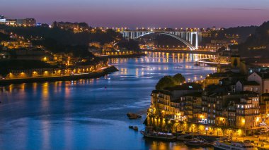 Day to night transition aerial view of the historic city of Porto, Portugal panoramic timelapse from the Dom Luiz bridge. Illuminated waterfront and curved river from above