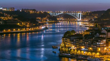 Day to night transition aerial view of the historic city of Porto, Portugal panoramic timelapse from the Dom Luiz bridge. Illuminated waterfront and curved river from above