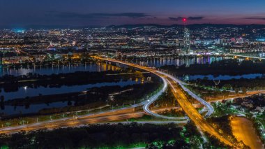 Viyana üzerinde gökdelenler, karayolu kavşağı ve Avusturya 'daki nehir kenarından geceye geçiş yapan hava panoramik manzarası. Akşam üstü Tuna Kulesi 'nden gün batımından sonra gökyüzü