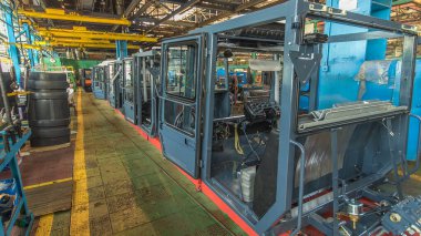 Konveyör montajı, traktörün gövdesini büyük endüstriyel fabrika zaman diliminde sahneleyecek. Kabin montajı, kurulum parçaları özel bir masada.