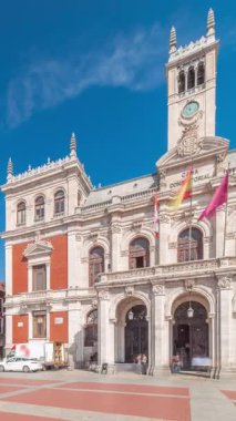 Panorama, Valladolid Plaza Belediye Başkanı Timelapse bayraklarıyla belediye binasının ön cephesini gösteriyor. Mavi gökyüzü ve şehrin göbeğindeki tarihi mimari. Yayalar bu merkez meydandan geçiyor..