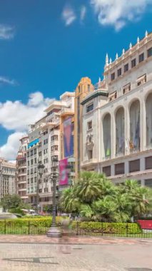 Valencia, İspanya 'da Belediye Meydanı Plaza del Ayuntamiento zaman atlaması hipervane. Büyük mimari, çiçek açan yeşillik ve bulutlu bir gökyüzünün altında su jetleri. İnsanlar canlı meydanda geziniyor..