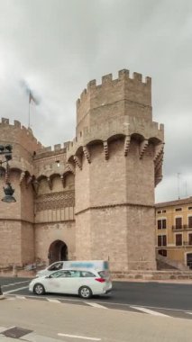 Serrans Kuleleri Torres de Serranos zaman atlaması. Valencia, İspanya 'da. Şehrin antik duvarlarından gelen büyük bir ortaçağ kapısı. Bulutlu bir gökyüzü altında hareketli bir sokak manzarası bu tarihi yeri çerçeveler.