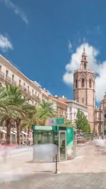 Valencia, İspanya 'da Plaza de la Reina' nın panoramik zaman atlaması. Tarihi bir kilise kulesi, hareketli kafeler ve sıcak Akdeniz semaları altında palmiyeleri olan merkezi bir çeşme..