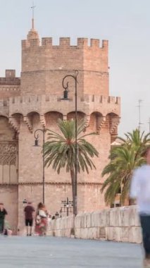 Serrans Kuleleri Torres de Serranos zamanapse Valencia, İspanya 'da. Şehrin antik duvarlarından gelen büyük bir ortaçağ kapısı. İnsanlar gün batımından önce tarihi bir dönüm noktasında köprüde yürüyorlar.