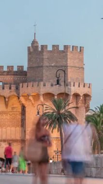 Serrans Kuleleri Torres de Serranos günden geceye Valencia, İspanya 'daki geçiş zamanı. Şehrin antik duvarlarından gelen büyük bir ortaçağ kapısı. İnsanlar tarihi bir dönüm noktasının yakınındaki bir köprüde yürüyorlar.