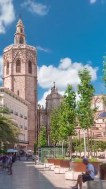 Valencia, İspanya 'daki Plaza de la Reina' nın panoramik zaman çizelgesi. Tarihi bir kilise kulesi, hareketli kafeler ve sıcak Akdeniz bulutlu gökyüzünün altında merkezi bir çeşme..