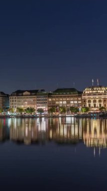 Binnenalster 'in Hamburg, Almanya' daki Belediye Binası ve Nikolai Kilisesi 'ndeki gece programı. Aydınlatılmış tarihi binalar yıldızlı bir gökyüzünün altındaki Alster Gölü sularına yansıyor. Manzaralı şehir manzarası