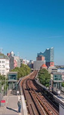 Almanya 'nın Hamburg kentindeki Landungsbrucken istasyonuna gelen trenler son sürat ilerliyor. Metroya binen insanlar mavi gökyüzünün altında Elbphilharmonie, liman ve marina ile panoramik manzara
