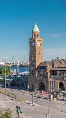 Hamburg, Almanya 'daki St. Pauli Piers Landungsbrucken' in uçuş zamanı. İkonik saat kulesi, yoğun sokak trafiği, limana yanaşmış gemiler ve mavi gökyüzünün altında panoramik manzaralar.
