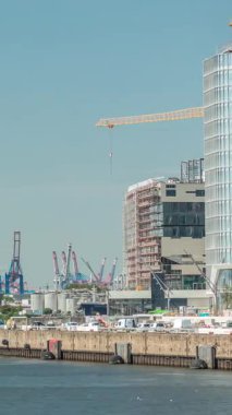 Hamburg kargo limanının zaman çizelgesi Elbe Nehri 'nde konteyner terminalleri, vinçler ve kargo gemileri sergileniyor. Tekneler ve gemiler modern binaların yanından geçerek dinamik bir deniz manzarası yaratıyorlar. Almanya