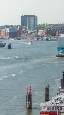 Almanya 'nın Hamburg kentinde Elbe nehir kenarının hava zaman çizelgesi. İskeleye yakın tekneler, Jan Fedder gezinti güvertesi, marina ve konteyner gemilerinin geçtiği manzara. Elbe Nehri kıyısındaki canlı şehir manzarası
